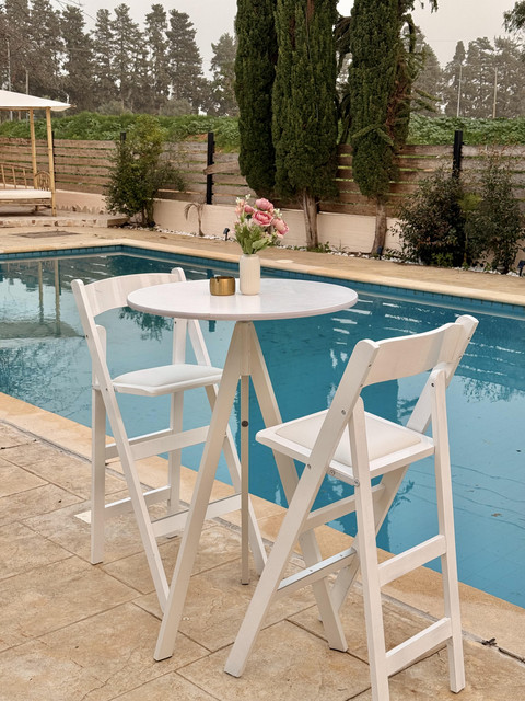 פינת בר לאירועים עם שולחן בר גבוה וכיסאות לבנים לצד בריכה